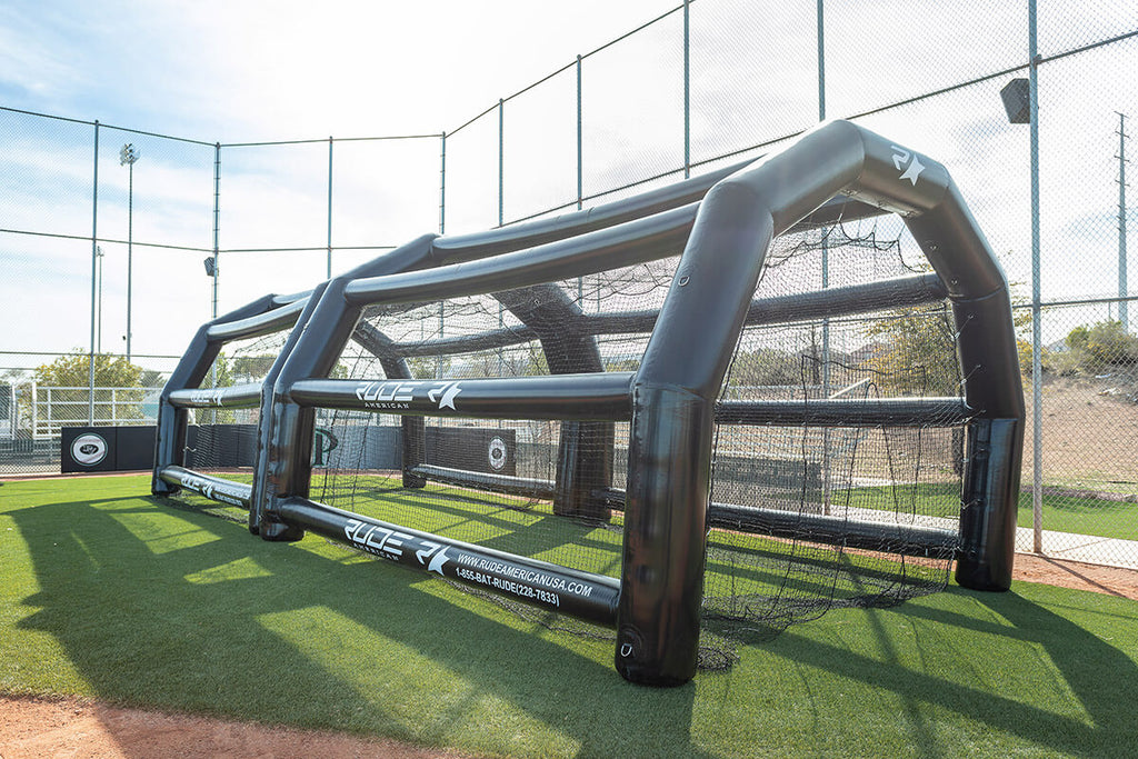 Rude American USA inflatable batting cage fully set up outdoors on a grass field, full side view showing the heat-sealed panel construction